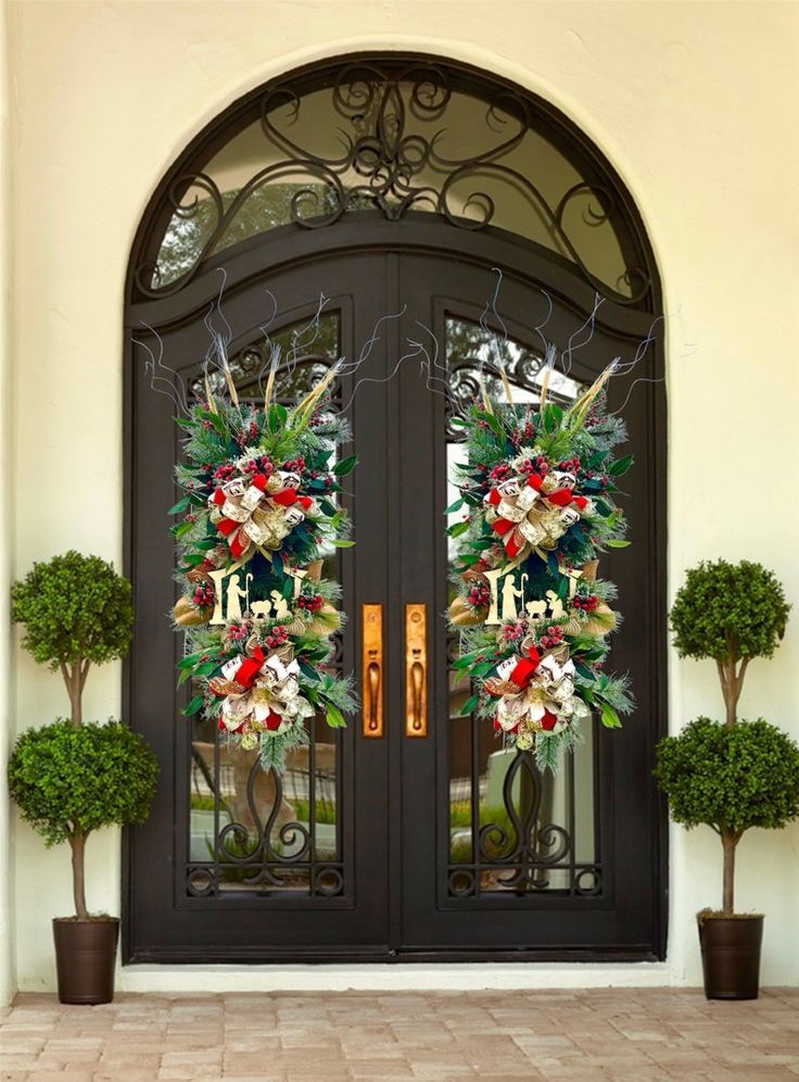 the front door is decorated with christmas wreaths and evergreen topiaries, along with two potted trees