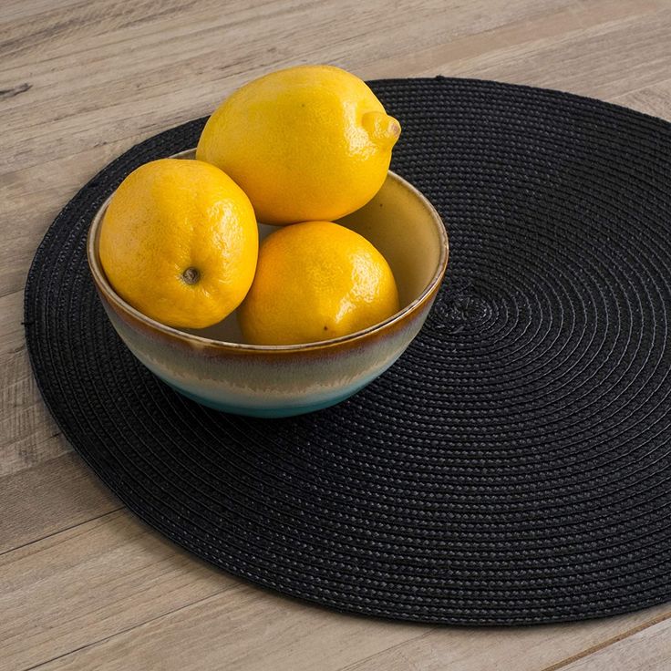 a bowl filled with lemons sitting on top of a black mat next to a wooden table