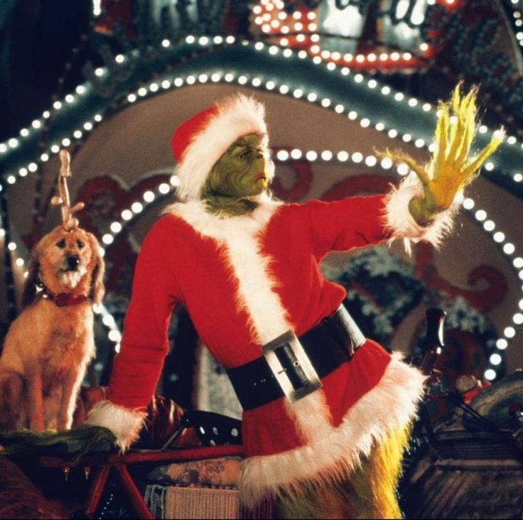 a man dressed as santa clause waves to his dog in front of christmas decorations and lights