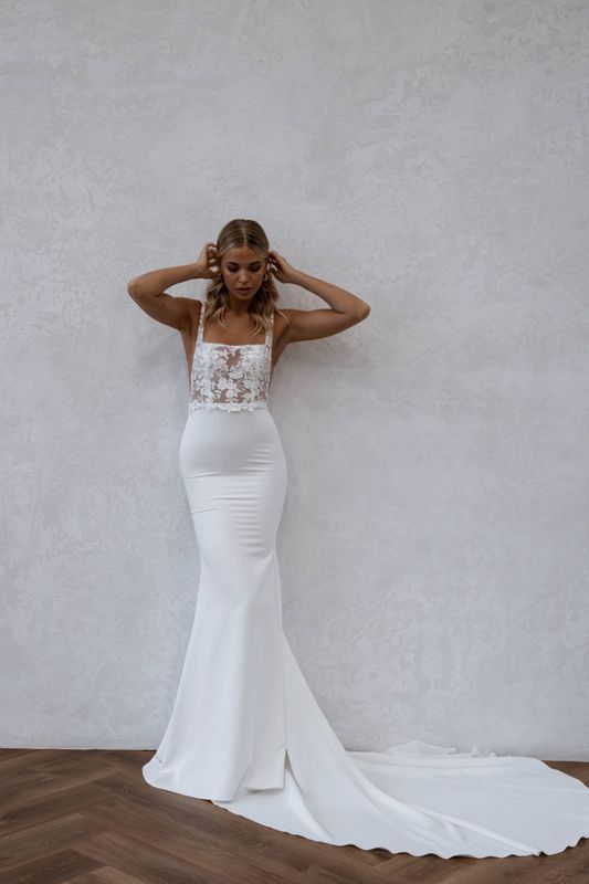 a woman in a white wedding dress standing against a wall with her hands on her head