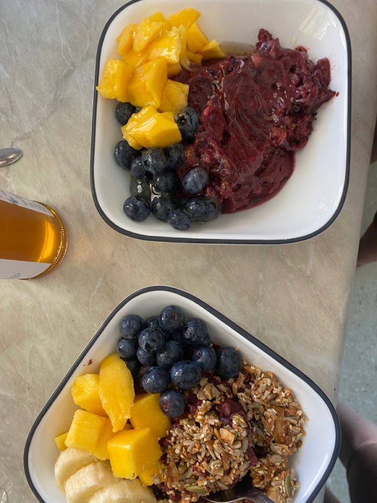 two bowls filled with fruit and granola next to a cup of tea on a table