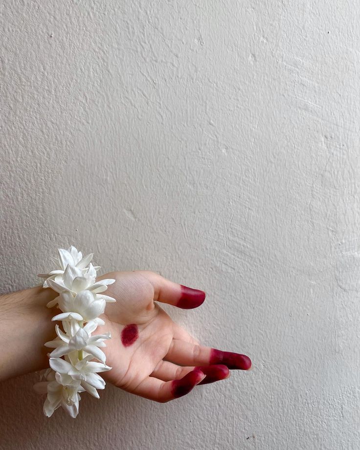 a woman's hand holding white flowers against a wall