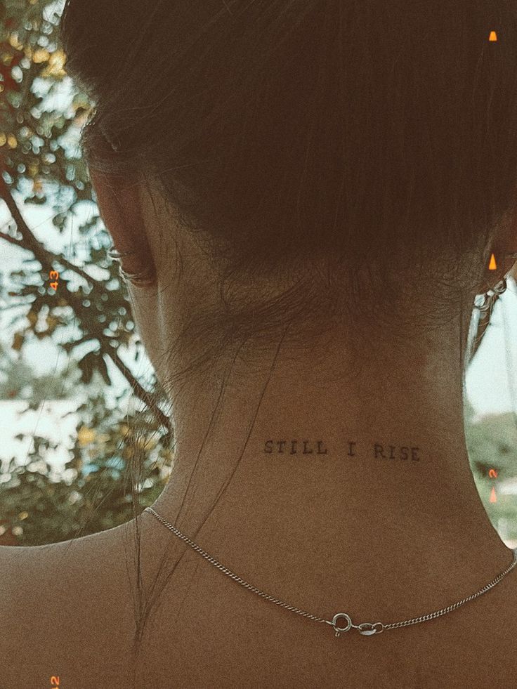 the back of a woman's neck has a small tattoo on it that says still i rise