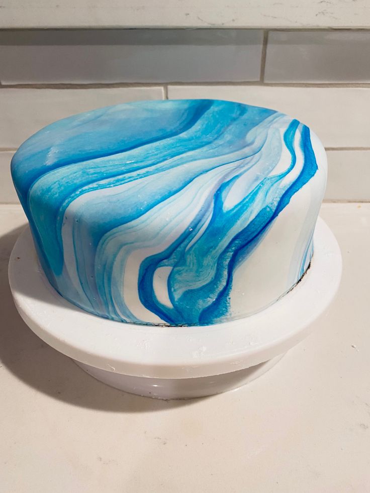 a blue and white cake sitting on top of a white plate next to a wall