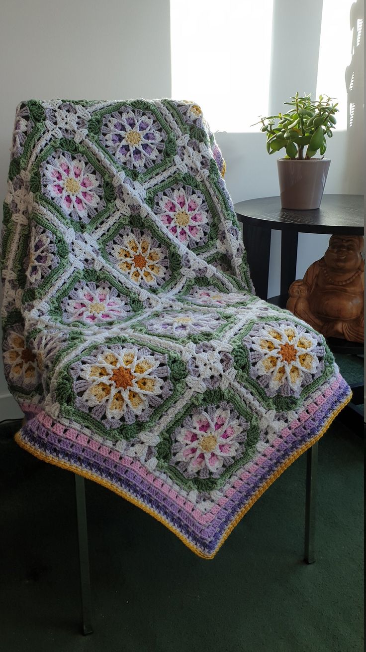 a crocheted granny blanket sitting on top of a chair next to a potted plant