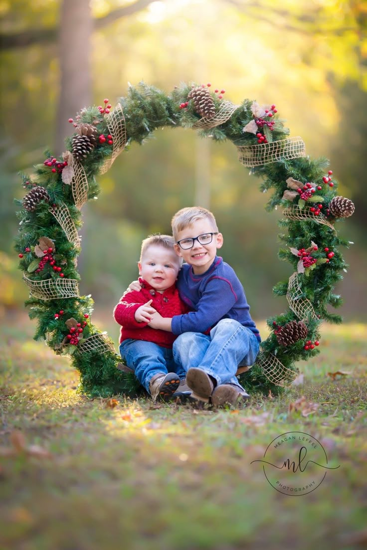 two young boys sitting in front of a christmas wreath