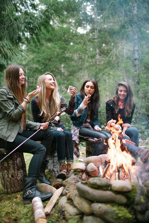 four women sitting around a campfire with their dogs