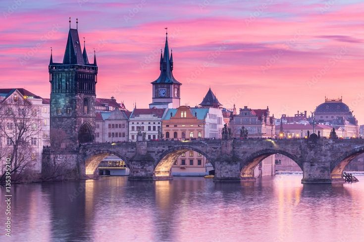 an old bridge over a river with buildings in the background at sunset, prague, czech