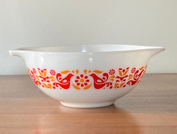 a white bowl with red and orange designs on it sitting on a table next to a wall