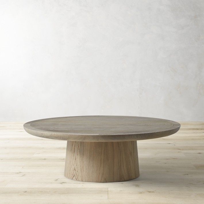 a round wooden table sitting on top of a hard wood floor next to a white wall