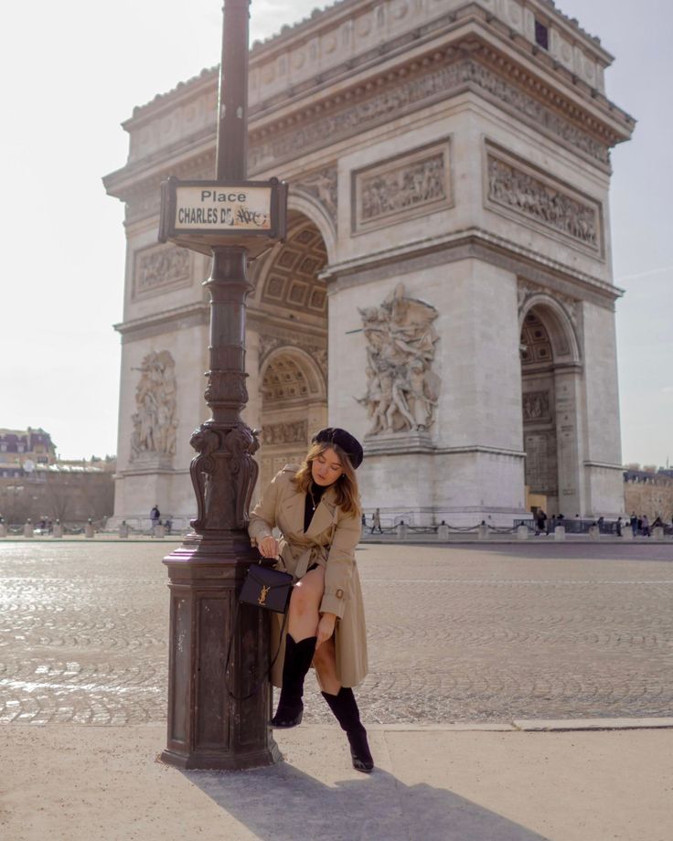 a woman leaning against a lamp post in front of the arc de trioe