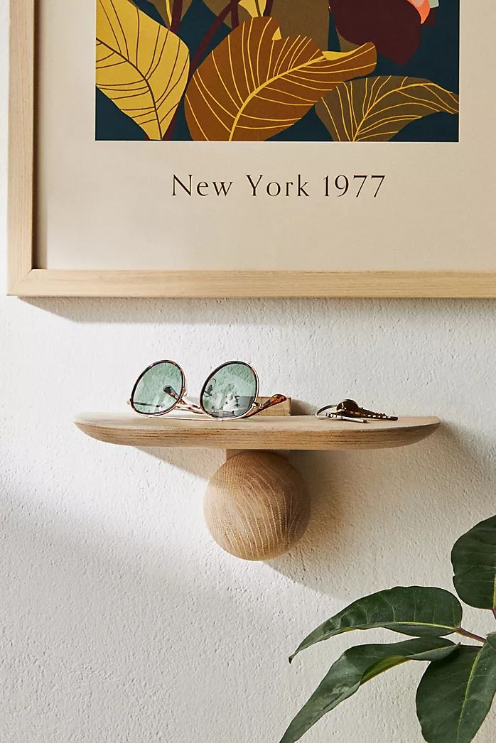 a wooden shelf with sunglasses on it next to a potted plant and framed photograph