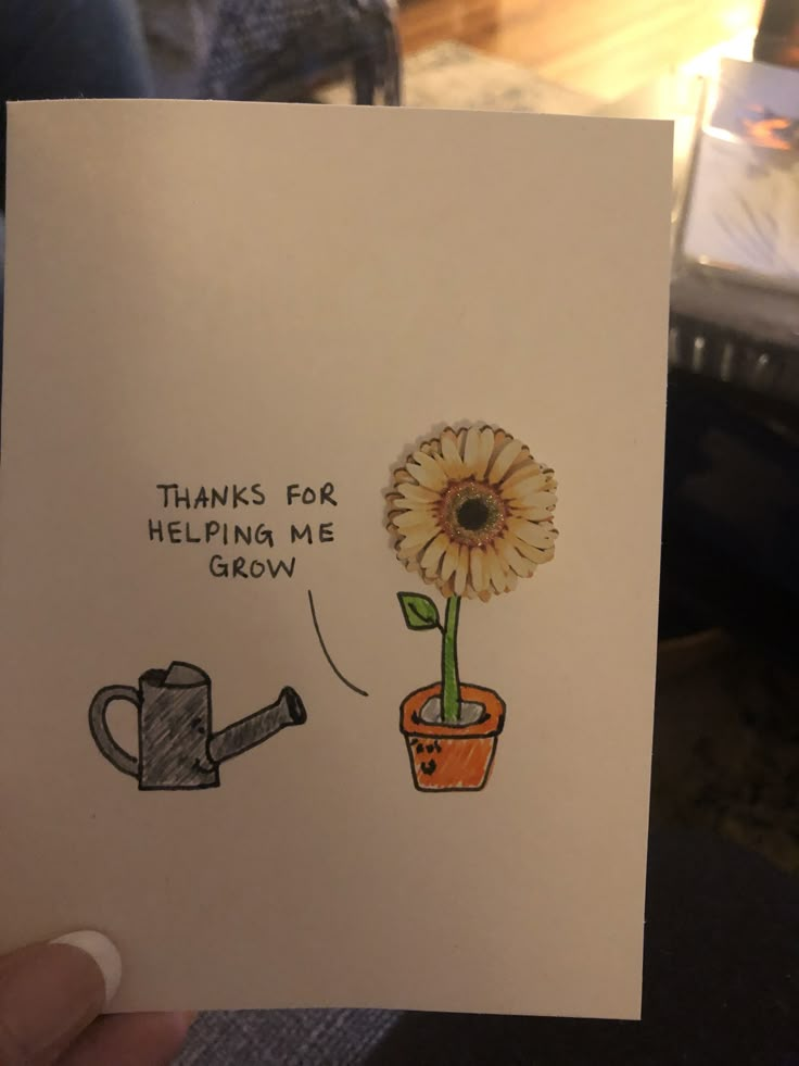 a person holding up a card with a drawing of a flower and watering can on it