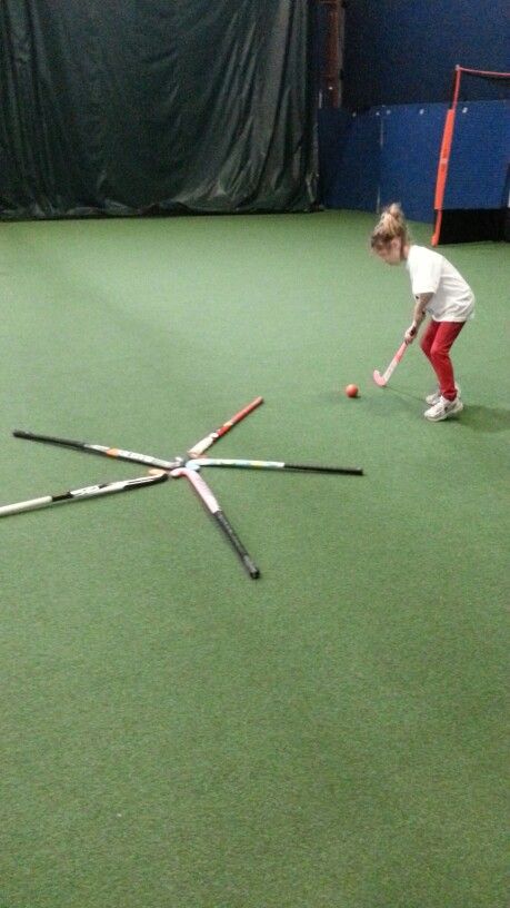 a young boy hitting a ball with a bat on an indoor field hockey rink area