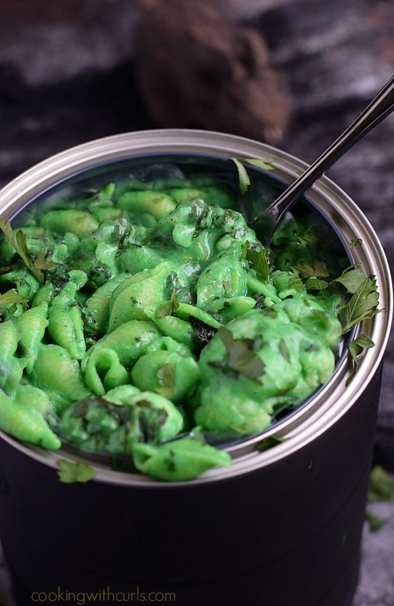 a pot filled with green food on top of a wooden table next to a spoon