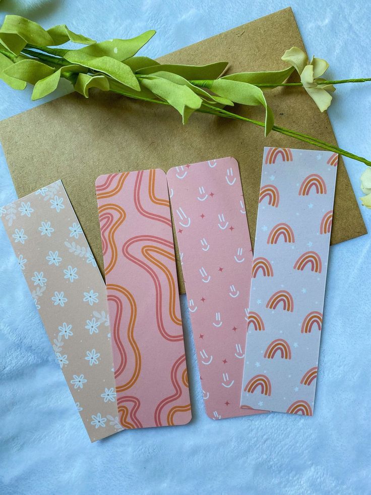 four different colored bookmarks sitting on top of a blue table cloth next to flowers