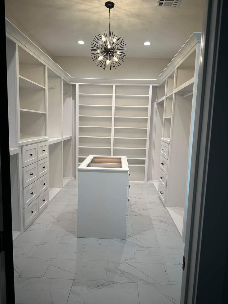 an empty walk in closet with white cabinets and marble flooring is seen from the doorway