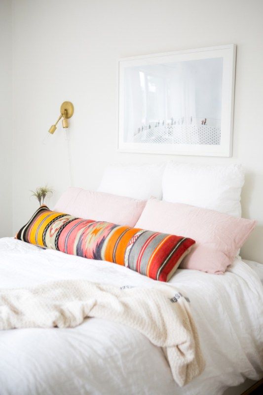 a white bed topped with lots of pillows next to a painting on the wall above it