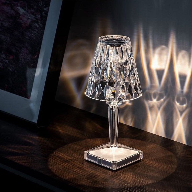 a crystal lamp sitting on top of a wooden table next to a framed photo and wall