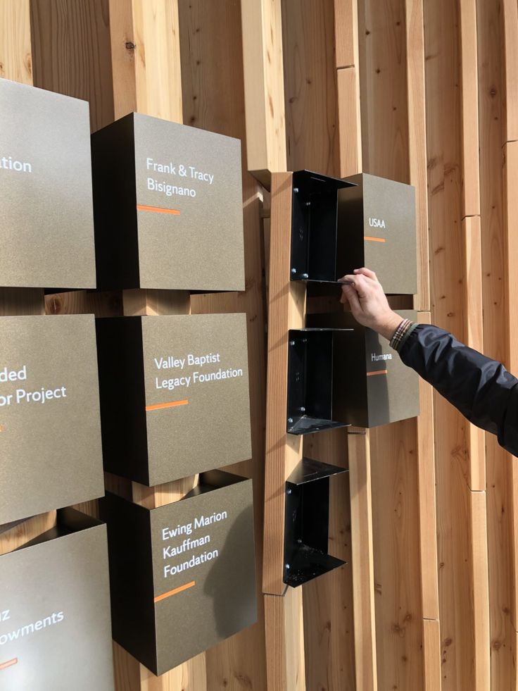 a man standing next to a wooden wall with several boxes on it and another person reaching for something