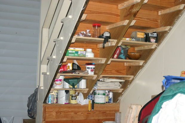 an under the stairs storage area with various items on shelves and in front of it