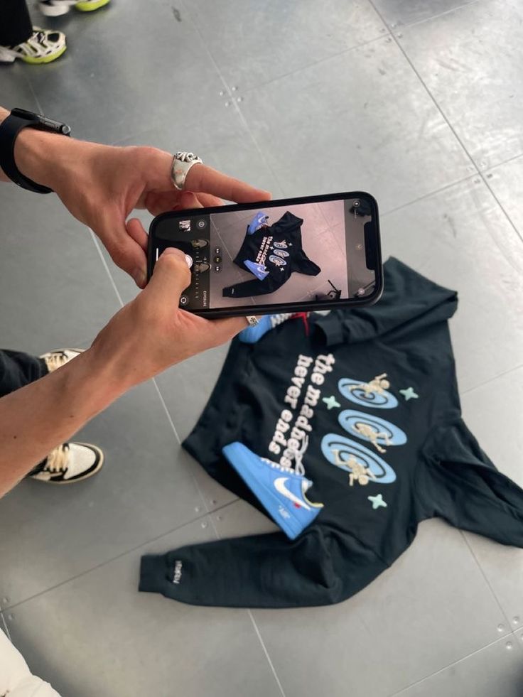 a person taking a photo with their cell phone while standing in front of a t - shirt