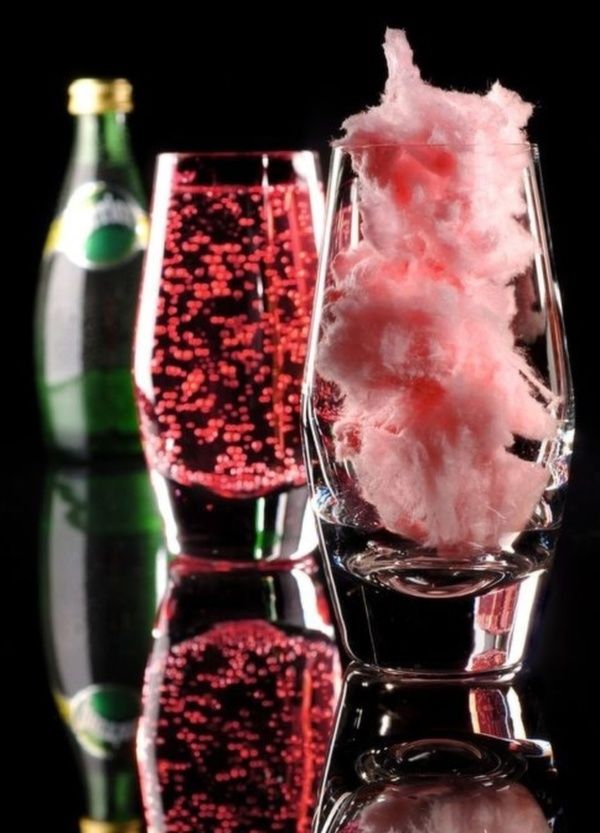 three glasses with pink cotton candy and two empty wine glasses next to each other on a reflective surface