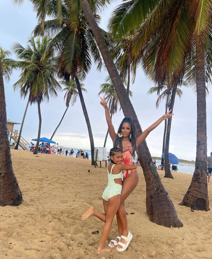 two girls are playing in the sand under palm trees at the beach with their arms around each other