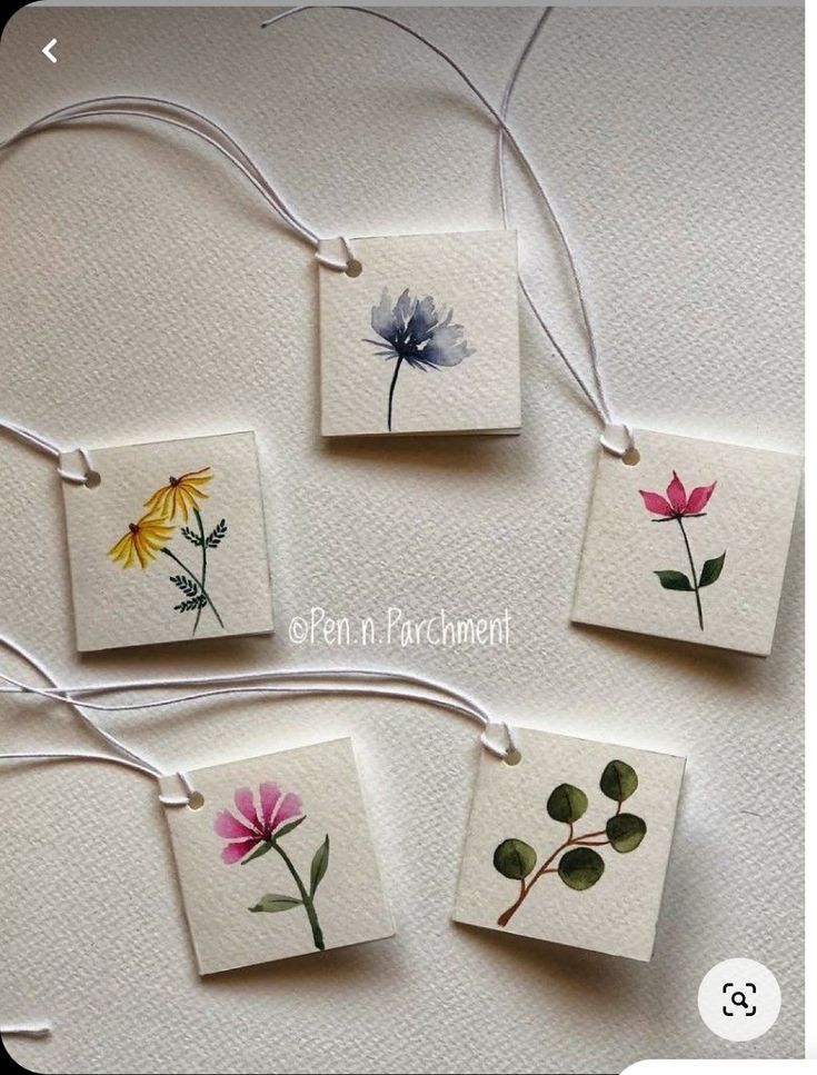 four small cards with flowers on them hanging from twine strings, one is white and the other is pink