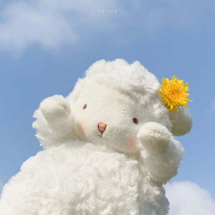 a white stuffed animal with a yellow flower in its ear and the sky behind it