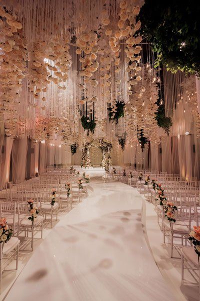 the aisle is lined with white chairs and decorated with flowers, greenery and hanging chandeliers