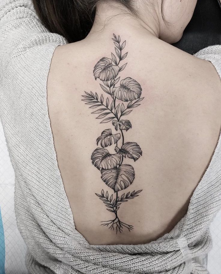 the back of a woman's neck with a plant tattoo on her left shoulder