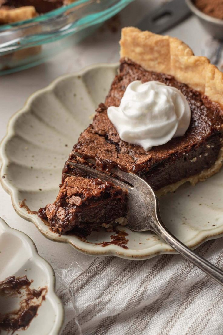 a slice of chocolate pie on a plate with a fork and bowl of whipped cream