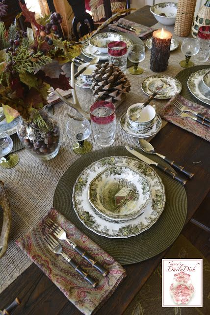 the table is set with dishes, silverware and pine cone centerpieces on it