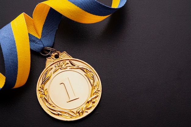 a gold medal with a blue and yellow ribbon around it on a black table top