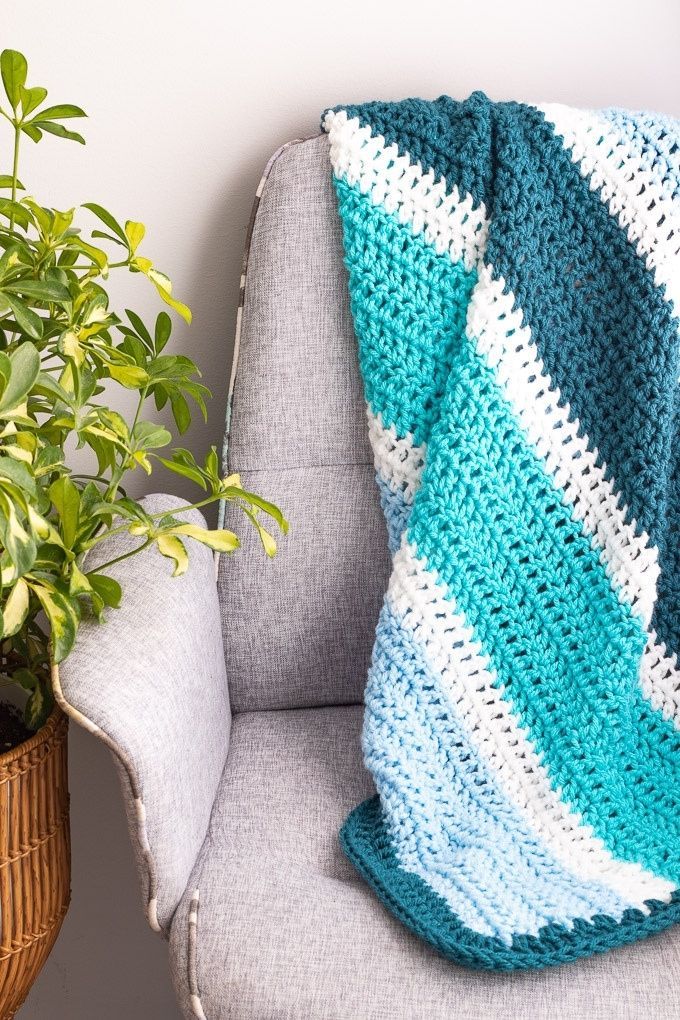 a blue and white crocheted blanket sitting on top of a chair next to a potted plant