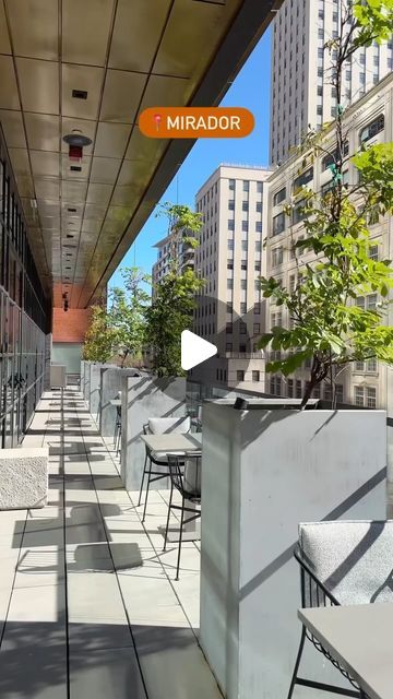 an outdoor patio with tables and chairs next to tall buildings in the distance, near a street sign that reads mirador