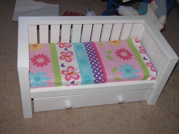 a white wooden bench with pink and blue sheets on it's bottom shelf, next to a stuffed animal