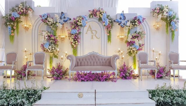 a stage set up for a wedding with flowers on the wall and chairs around it