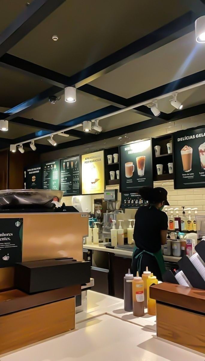 a person standing in front of a counter with drinks on it and menus hanging from the ceiling