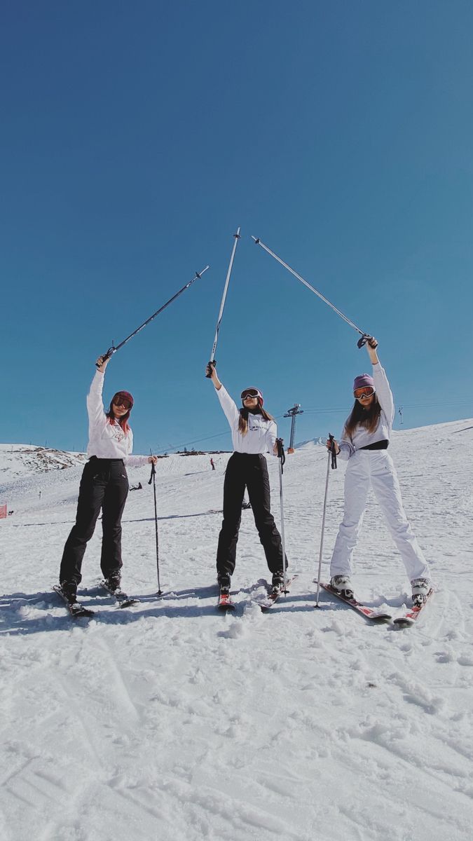 three people on skis holding their poles up in the air