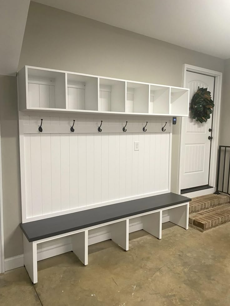 a white bench sitting in the middle of a room next to a wall mounted coat rack