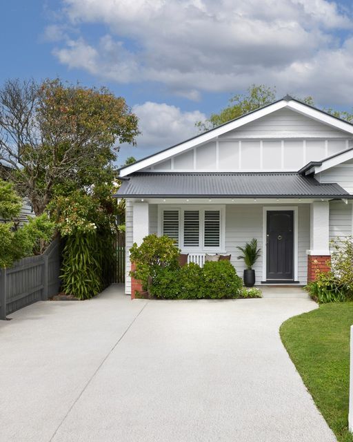 a white house with black shutters on the front and side doors is surrounded by greenery