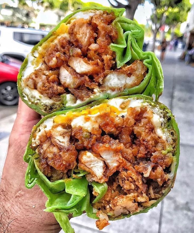 a person holding up two stuffed peppers with meat and cheese on them in the street