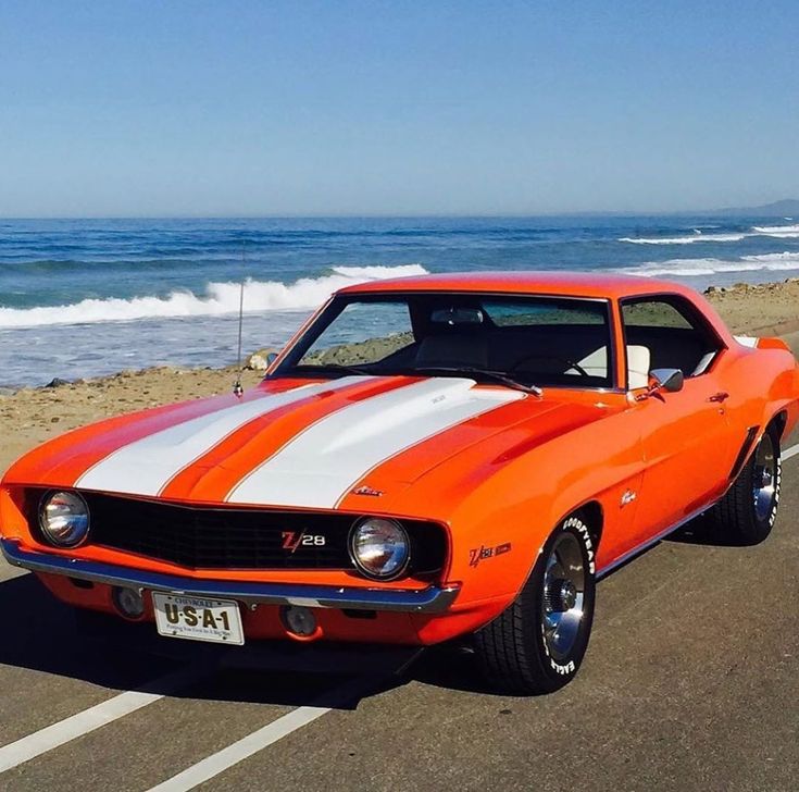 an orange and white muscle car parked on the beach