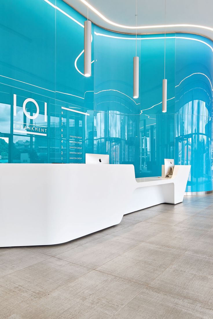 an empty reception area with blue walls and white counter tops on the floor, along with hanging lights