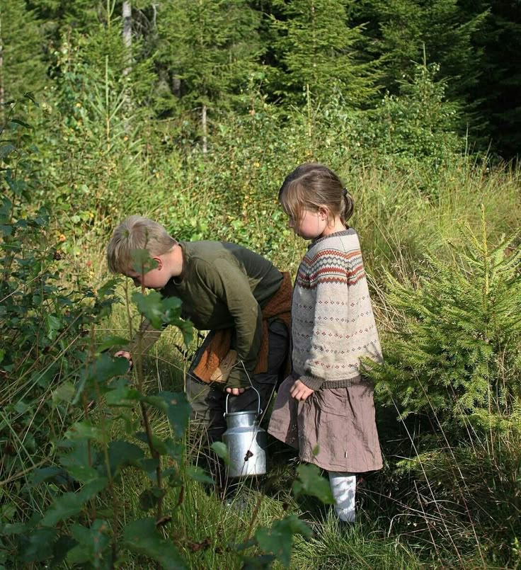 two young children are standing in the woods with buckets on their heads and looking at something