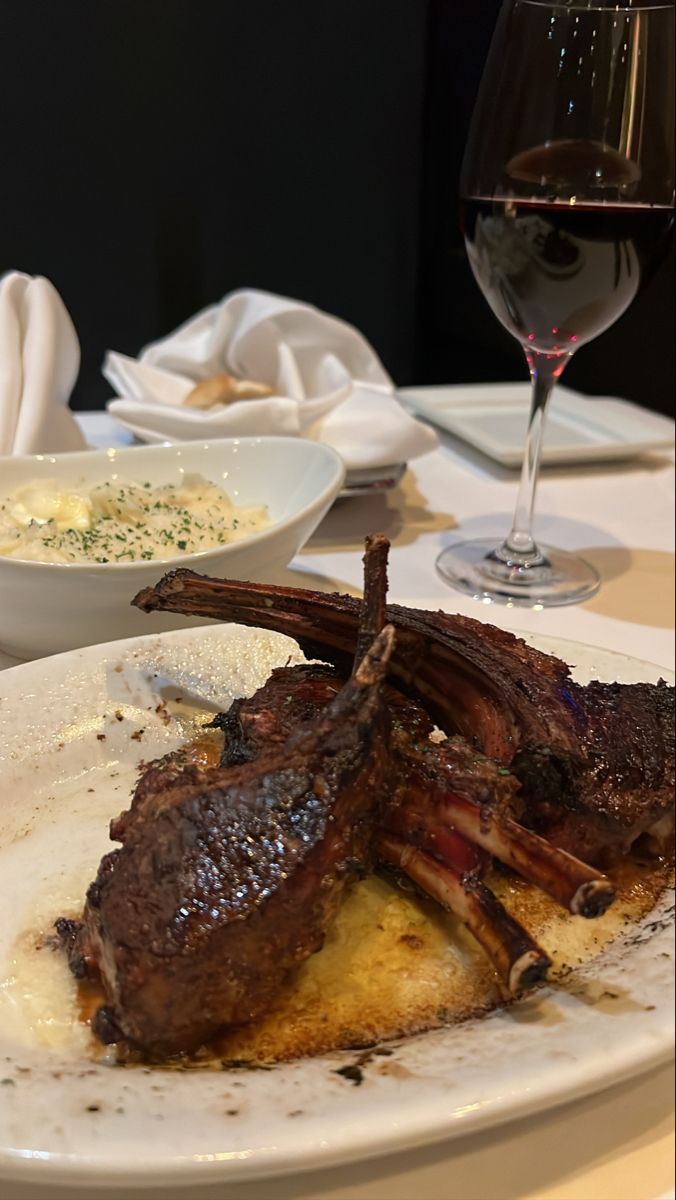 a white plate topped with meat next to a glass of wine