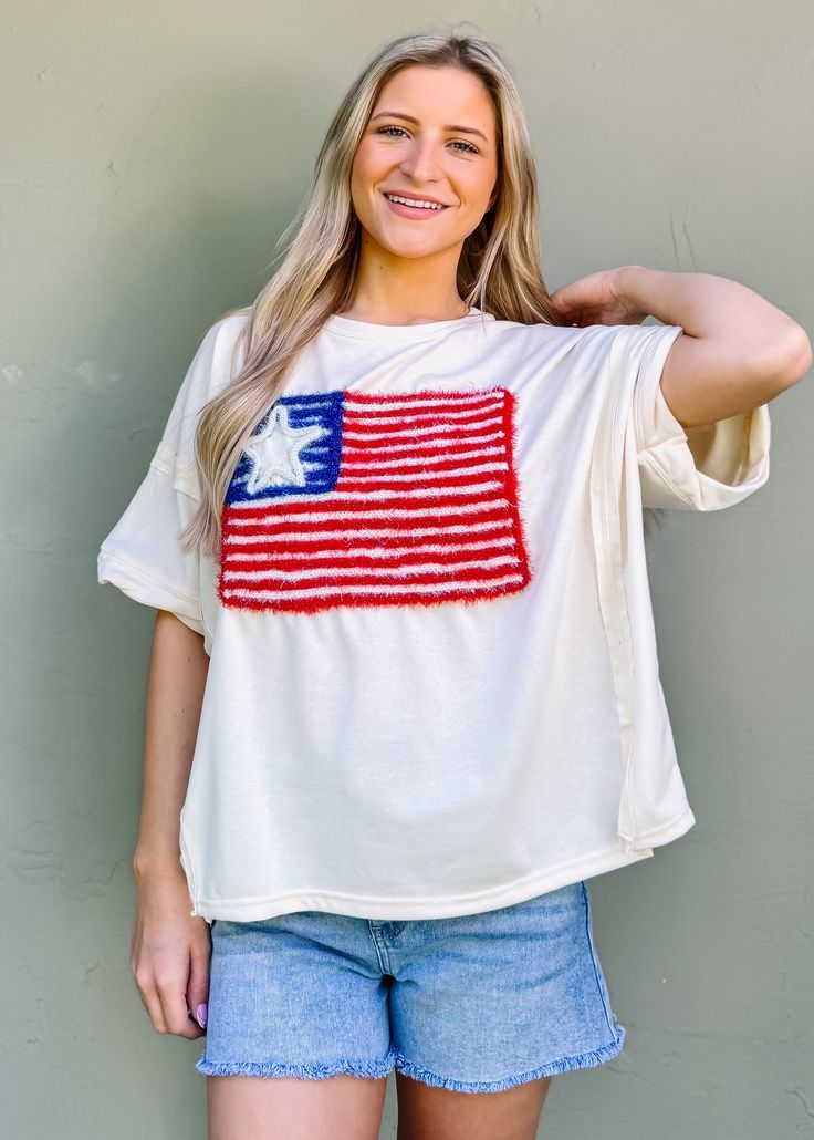 This patriotic tee features a sparkling USA flag embroidery, perfect for Fourth of July celebrations. With a girly and fun touch, it's a must-have for summer outings. Show off your love for America in a unique way with this American Flag Lurex Embroidery Tee. Oversized/ loose fit Round neckline Pull on fit Color: Cream Lurex embroidery Not lined 85% cotton 15% polyester Fabric has little stretch Cotton Tops With Star Patch For Spring, Patriotic American Flag Tops For Spring, American Flag Crew Neck Top For Spring, Americana Tops With American Flag For Independence Day, Americana Flag Print Tops For Spring, Summer Cotton Tops With Flag Print, Cotton Flag Print Tops For Summer, Patriotic Crew Neck Top For Summer, American Flag Print Tops For Summer