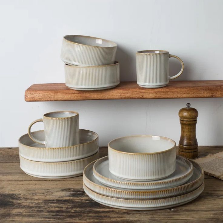 white and gold dinnerware sitting on top of a wooden shelf